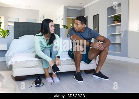 Coppia afroamericana seduta sul letto, preparandosi per l'allenamento a casa, sorridendo Foto Stock
