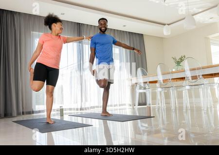 Accoppiatevi praticando yoga insieme a casa, bilanciandovi su una gamba e sorridendo Foto Stock