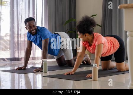 Coppia afroamericana che fa yoga insieme sui tappetini a casa, sorridente e rilassata Foto Stock