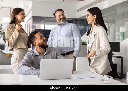 Felici colleghi diversi in piedi e seduti insieme sul posto di lavoro Foto Stock