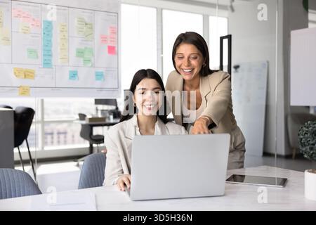 Due allegri amici multietnici dell'ufficio che si divertono con il computer portatile Foto Stock