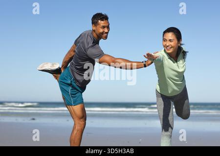 Coppia che si allenano sulla spiaggia, si equilibrano su una gamba e sorridono insieme Foto Stock