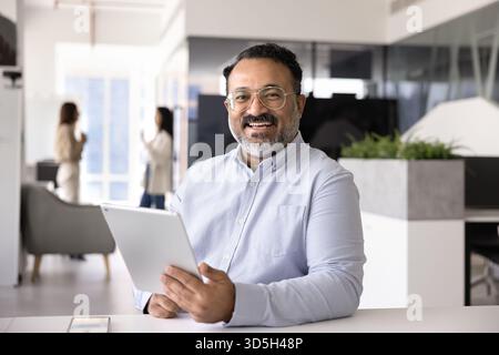 Felice uomo d'affari indiano anziano che posa per un ritratto sul posto di lavoro Foto Stock