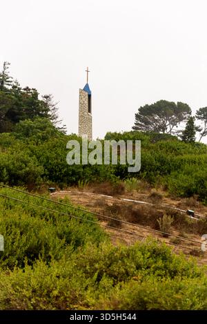 Il caratteristico campanile in pietra della Wayfarers Chapel sorge sopra una lussureggiante collina verde a Palos Verdes, California, segnata da una guglia a croce. Foto Stock