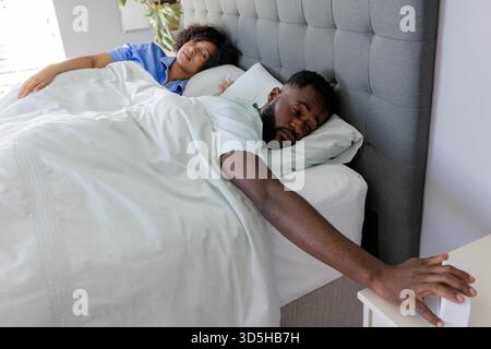 Uomo afroamericano che sta cercando la sveglia mentre si sveglia accanto al partner Foto Stock
