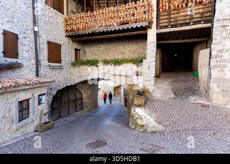 Due persone camminano per la strada pittoresca e le belle case tradizionali del villaggio di rango in provincia di Trento, Trentino alto Adige, Italia Foto Stock