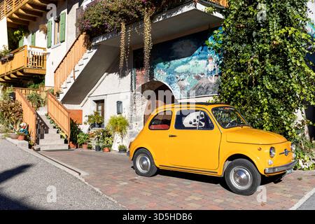 FIAT 500 giallo vecchio stile parcheggiato all'esterno delle tradizionali vecchie case del villaggio rango in provincia di Trento, vicino al lago di Garda in Italia Foto Stock