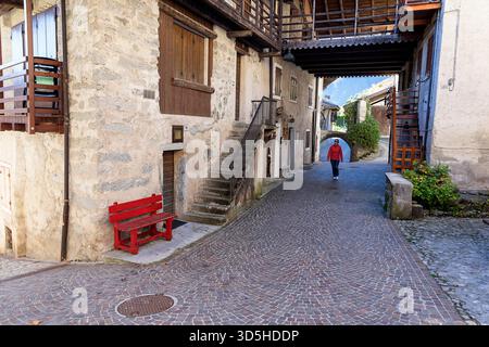 Donna che cammina per la strada pittoresca e le belle case tradizionali del villaggio di rango in provincia di Trento, Trentino alto Adige, Italia Foto Stock
