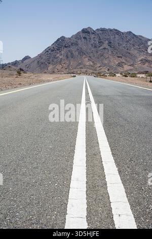 Strada asfaltata con doppia linea bianca che si estende verso un paesaggio desertico e montagne lontane Foto Stock