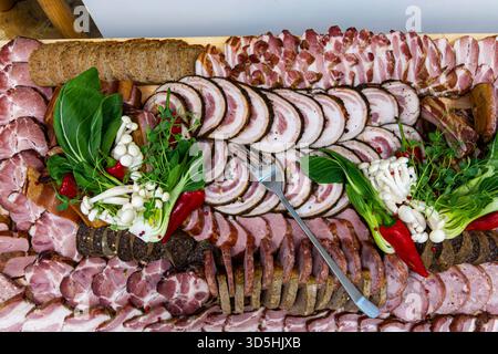 Tagliere di salumi con carni a fette e verdure. Vista dall'alto di un elaborato piatto di salumi con affettati assortiti, salsicce e verdure a foglia verde Foto Stock
