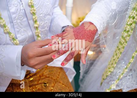 Un primo piano della mano della sposa decorata con henné è indossato da un anello nuziale da un uomo Foto Stock