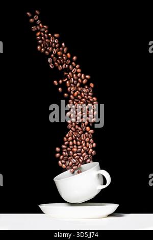 I chicchi di caffè cadono in una tazza Foto Stock