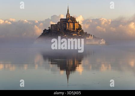 Una splendida vista di Mont Saint-Michel che sorge sopra le acque nebbiose durante l'alba. La luce calda mette in risalto gli intricati dettagli dell'arcata storica Foto Stock