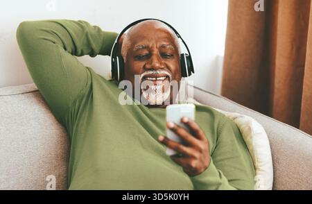L'uomo anziano ama ascoltare musica al telefono mentre si rilassa a casa in un ambiente accogliente Foto Stock