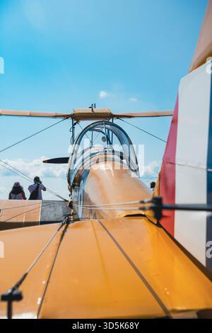 Visuale ad angolo basso dal retro del biplano giallo d'epoca che mostra la cabina di pilotaggio aperta, la fusoliera, l'ala superiore e le pale del rotore. Ripresa da dietro il sedile pilota guardando f Foto Stock