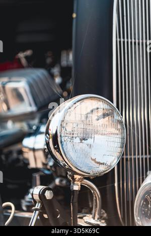 Faro cromato montato su un'asta calda vintage con barre della griglia verticali visibili. Profondità di campo ridotta con sfondo sfocato che mostra una classe aggiuntiva Foto Stock