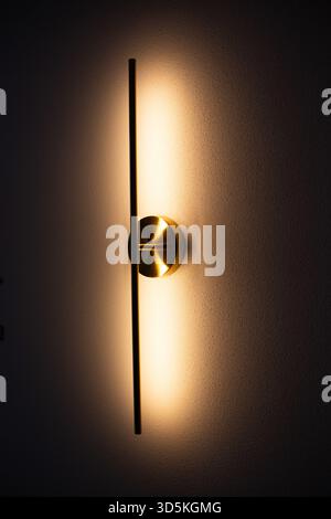 Questa applique moderna e minimalista dal design lineare irradia una calda luce soffusa su una parete testurizzata, creando un'atmosfera accogliente. Foto Stock