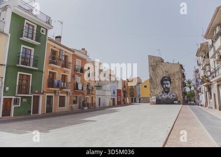 11.09.2019, Villajoyosa, Spagna: Strada colorata con tradizionali case mediterranee e un grande murale di un uomo barbuto su un muro intemprato sotto la c Foto Stock