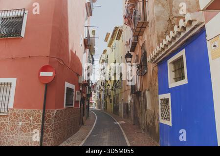 11.09.2019, Villajoyosa, Spagna: Stradina stretta e tortuosa con colorati edifici mediterranei, balconi in ferro battuto e un cartello di divieto di ingresso sotto la luce Foto Stock