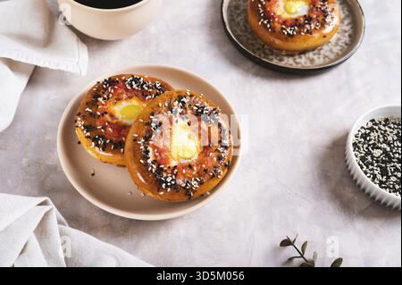 Uovo con pomodoro e semi di sesamo cotti in bagel su un piatto sul tavolo Foto Stock