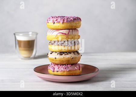Ciambelle glassate su piatti e caffè latte o cappuccino con schiuma di latte in una tazza di vetro resistente al calore. Messa a fuoco selettiva Foto Stock