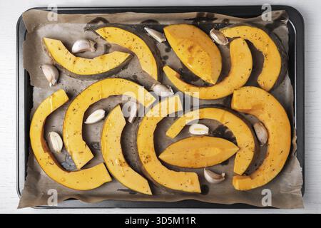 Grandi pezzi di zucca sono disposti su carta pergamena su foglio da forno con olio d'oliva, aglio ed erbe secche. Cibo sano e vegetariano. Selettivo f Foto Stock