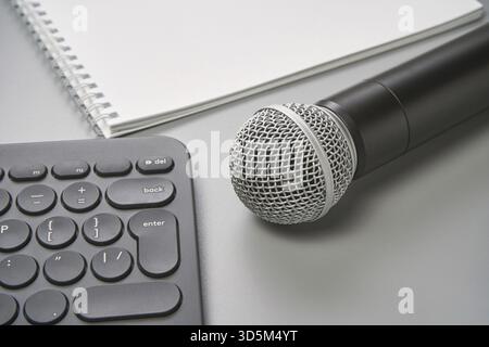 Concetto di podcast. Quaderno bianco con foglio bianco. Microfono nero, notebook e tastiera. Audiolibri e podcasting. Tecnologia audio. Tè della scuola a casa Foto Stock