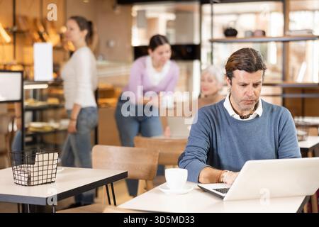 Serio uomo di mezza età seduto al tavolo, con un computer portatile e una tazza di tè nella caffetteria Foto Stock