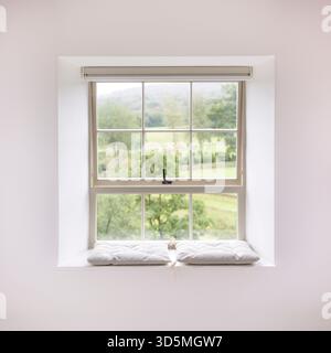 Tradizionale finestra a telaio in legno con un sedile imbottito, adagiata su pareti bianche in una casa del Regno Unito, con una vista panoramica della campagna Foto Stock