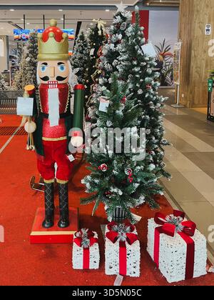 Balikpapan, Indonesia - 16 novembre 2025. Una grande statua dello Schiaccianoci e alberi di Natale artificiali, circondati da scatole regalo decorative, come Foto Stock