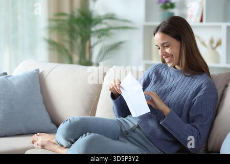 Donna felice in busta blu aperta seduta su un divano a casa Foto Stock