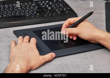 mani maschili che disegnano e ritoccano l'immagine sul computer pc, utilizzando un tablet grafico digitale e una penna stilo alla scrivania dell'ufficio. Foto Stock