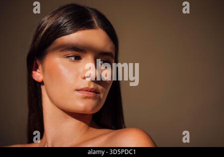 Giovane donna dai lunghi capelli scuri, illuminata da una luce naturale soffusa, guarda con attenzione, ombre che esaltano le sue caratteristiche, creando un ambiente sereno e introspo Foto Stock