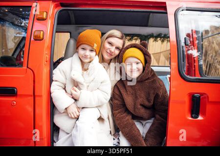 Donne e due bambini si godranno un momento accogliente in un veicolo rosso brillante, vestito con caldi abiti invernali, che irradiano gioia e amore familiare Foto Stock