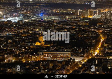 Vista aerea dell'Dôme des Invalides illuminato che risplende calorosamente tra gli scuri arazzi urbani sotto il cielo notturno, Parigi, Ile-de-France, Francia. Foto Stock