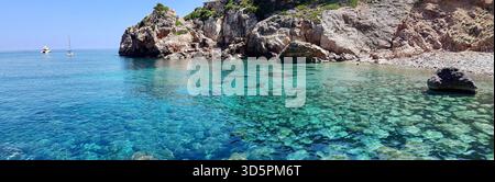 Ampia vista panoramica di una isolata baia mediterranea con acque cristalline blu turchese, incorniciate da aspre rocce costiere, Maiorca, Spagna Foto Stock