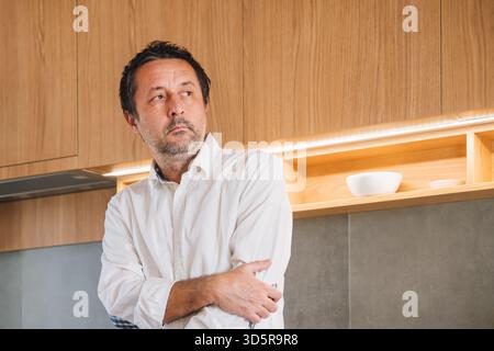 Un uomo maturo e premuroso che si trova in una cucina moderna e che guarda lontano dalla contemplazione. Messa a fuoco selettiva. Foto Stock