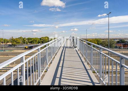 Una vista frontale che cattura l'eleganza del cavalcavia pedonale in metallo bianco che si estende in una curva delicata sull'autostrada Foto Stock