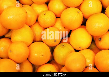 Immagine di sfondo ravvicinata di una grande pila di arance mature appena raccolte, che mostrano texture e colori vivaci. Foto di alta qualità Foto Stock