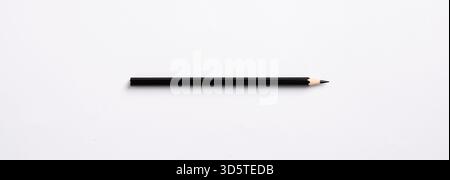 Primo piano minimalista di una matita nera appoggiata su una superficie bianca incontaminata, che enfatizza la semplicità e il potenziale di creatività Foto Stock