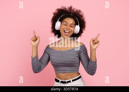 Gioiosa donna afroamericana con cuffie wireless che ballano e ascoltano musica Foto Stock
