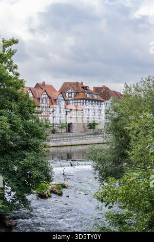 Vista panoramica delle tradizionali case a graticcio lungo il fiume con una piccola cascata nella città vecchia di Hann. Münden, bassa Sassonia, Germania Foto Stock