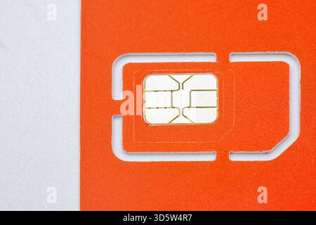 Vista ravvicinata di una scheda SIM mobile arancione brillante con punti di contatto chip oro metallico, visualizzata su una superficie bianca. Tecnologia moderna delle telecomunicazioni Foto Stock