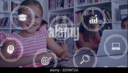 Tenendo in mano un tablet, una ragazza in camicia rosa seduta in classe, scaffali, un ragazzo che usa un laptop, icone HUD. Studenti, libreria, lavoro di squadra, apprendimento, dispositivi, col Foto Stock