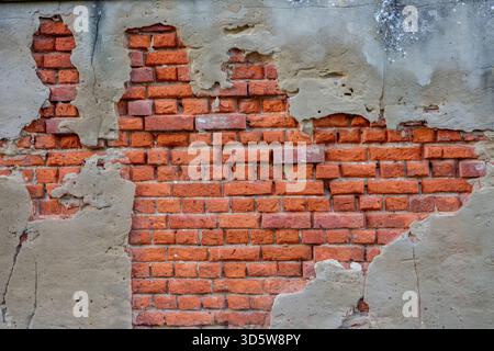 Parete danneggiata con rendering che cade dal muro di mattoni rossi. Rendering che fuoriesce dalla parete a causa dell'umidità. Foto Stock