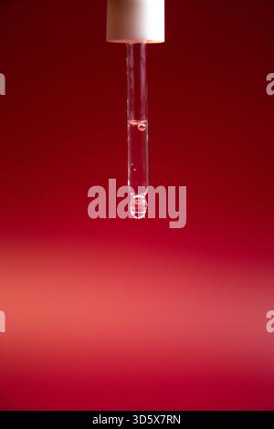 Il contagocce liquido è elegantemente sospeso a mezz'aria su un suggestivo sfondo rosso, che mostra il Foto Stock