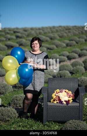 Una festa gioiosa si svolge in un lussureggiante campo di lavanda, mentre una donna tiene dei palloncini colorati e una torta, incarnando la felicità e l'essenza di Lives preci Foto Stock