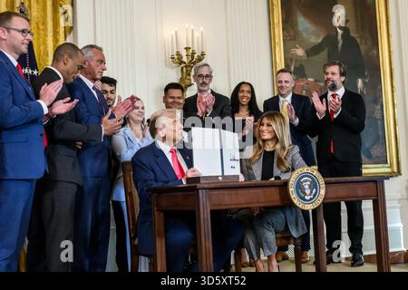 Il presidente Donald Trump mostra il firmato che promuove il futuro ordine esecutivo nella East Room della Casa Bianca con la First Lady Melania Trump e applaude gli ospiti. Washington, D.C., 13 novembre 2025. Per gentile concessione della Casa Bianca. Foto Stock