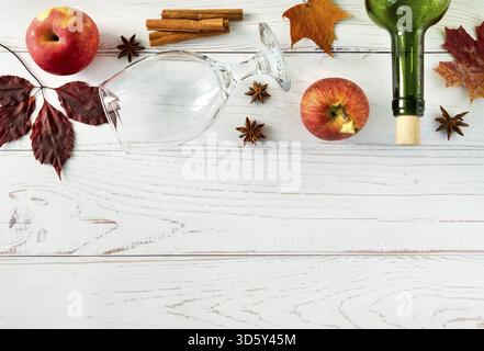 Mele rosse fresche e succose, spezie, bottiglia e bicchiere per sidro su una superficie di legno chiaro con foglie autunnali. Orientamento orizzontale, messa a fuoco selettiva Foto Stock