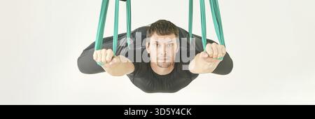 La persona maschile fa esercizio di lezioni di yoga sull'amaca. Meditazione in aria calma. Allenamento in studio per principianti Aero. Stile di vita degli uomini. Ragazzo che allena la posa zen. Verde. Amaca Foto Stock